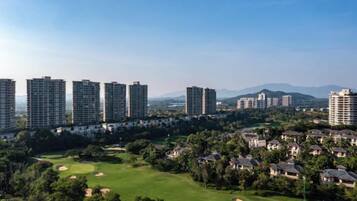 A residential area with high-rise buildings, a golf course, and a hilly landscape in the background.