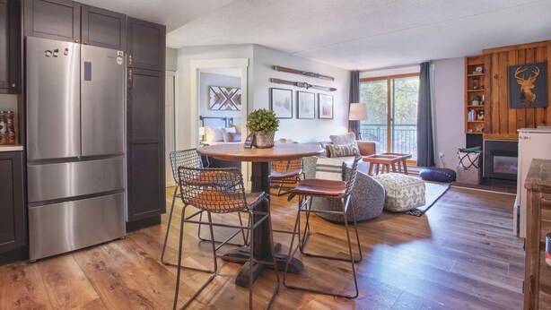 A modern kitchen with a stainless steel refrigerator, wooden flooring, and a dining area with a round table and wire mesh chairs. - Ski in/Ski out and 1 block from Main Street! (Breckenridge)