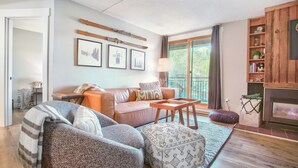 A cozy living room with a leather sofa, a patterned ottoman, and a wooden coffee table. There is a fireplace and a bookshelf with various items. - Ski in/Ski out and 1 block from Main Street! (Breckenridge)
