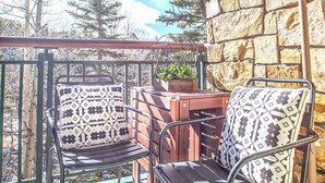 A balcony with two metal chairs and a table, a stone wall, and a view of trees and sky. - Ski in/Ski out and 1 block from Main Street! (Breckenridge)