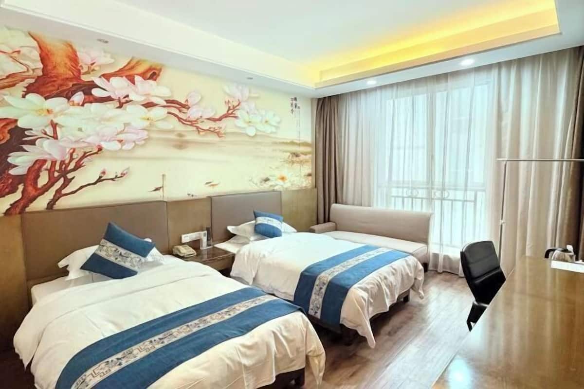 Una habitació d'hotel amb dos llits, un escriptori i una finestra gran amb cortines.