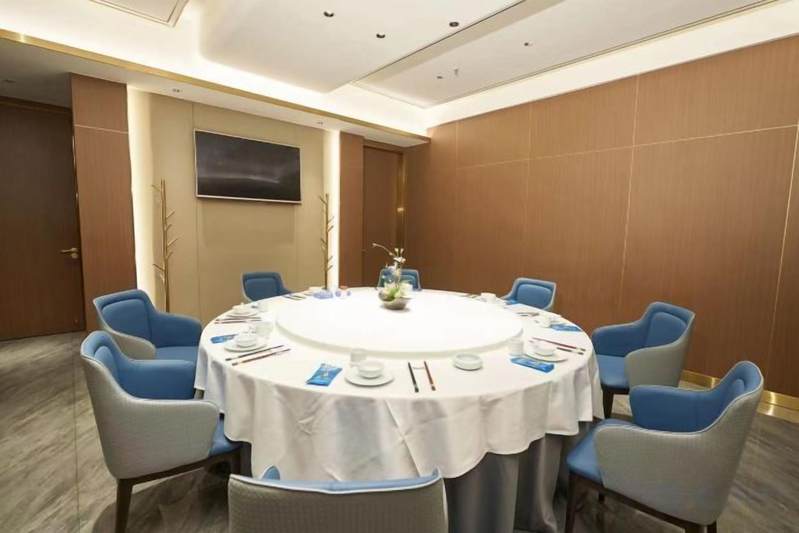 A conference room with a round table, blue chairs, and a white tablecloth.
