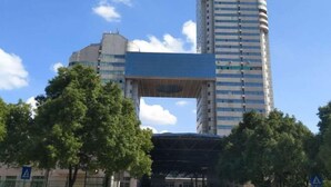 A tall building with a distinctive blue overhang structure in front. - Mango City Inn (Moon Lake Park North Metro · Window of the World Mango Pavilion) (Changsha)