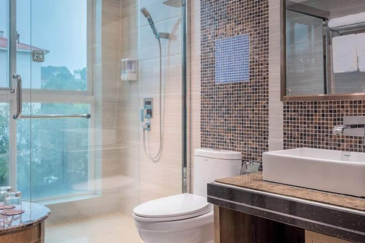 Un bany modern amb plat de dutxa de vidre, vàter blanc, un mirall gran i un lavabo amb taulell.