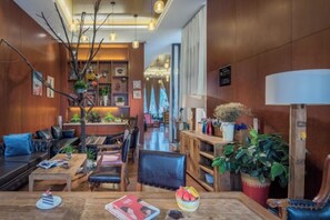 Um saguão de hotel moderno com balcão de recepção em madeira, áreas de estar confortáveis e diversas plantas.