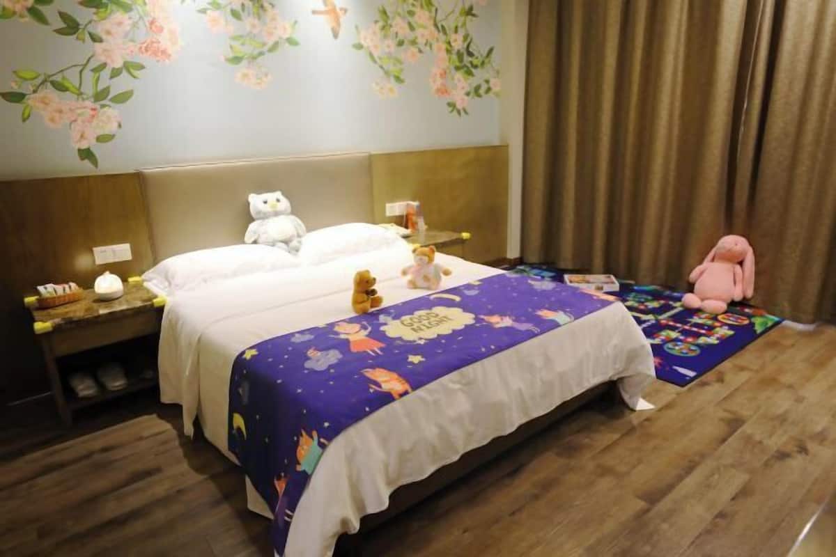 Una habitació d'hotel amb un llit, una vetusta, un os de peluix, una cadira rosa i un mural floral a la paret.
