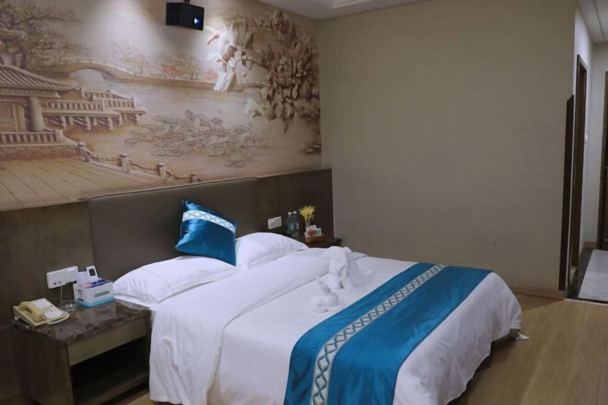 A hotel room with a bed, a nightstand, a wall mural, and a TV.