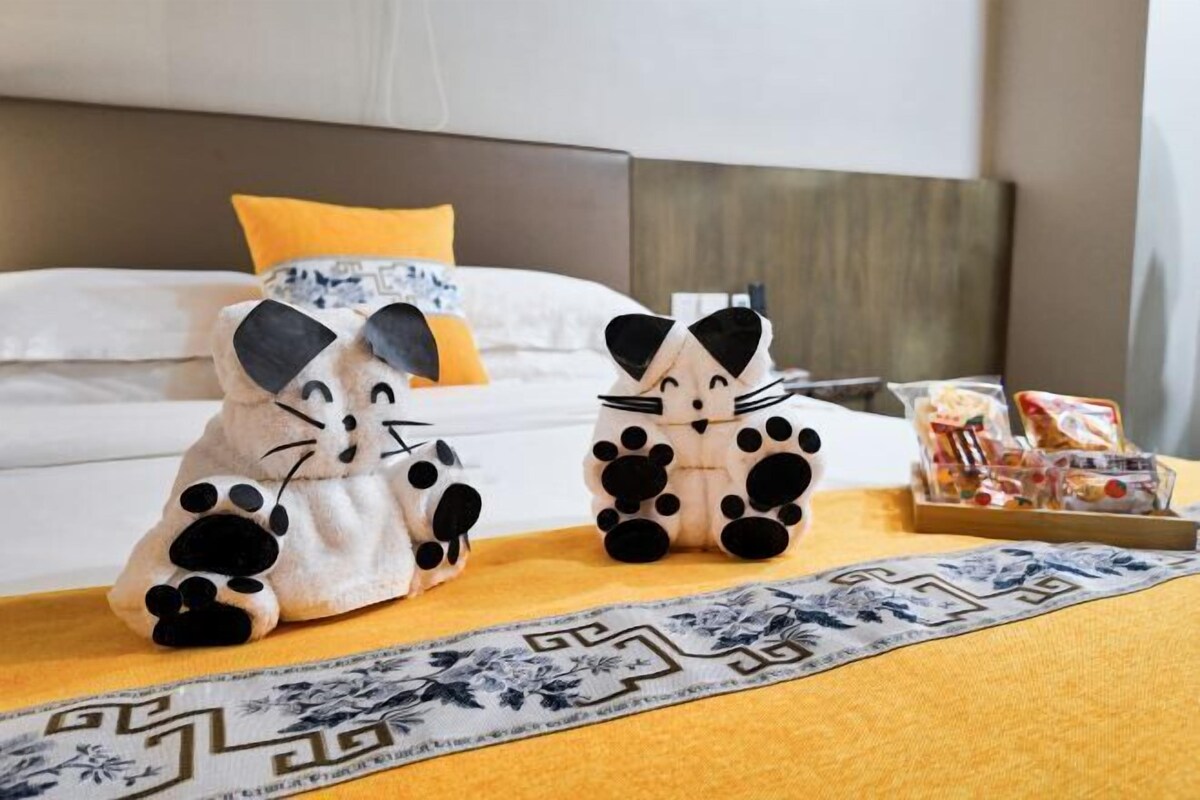 A bed with a headboard, a yellow throw blanket, and two plush toys on the bed.