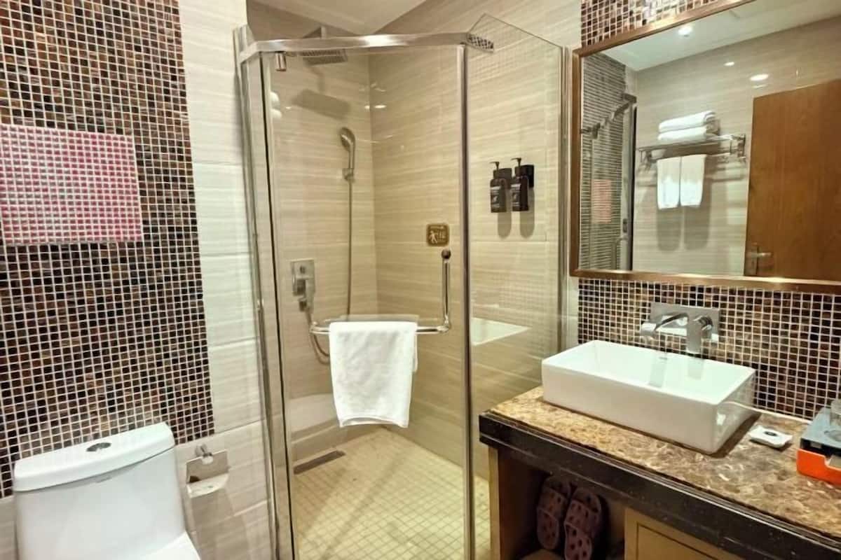 Un bany modern amb dutxa de vidre, un lavabo blanc i un mirall gran.