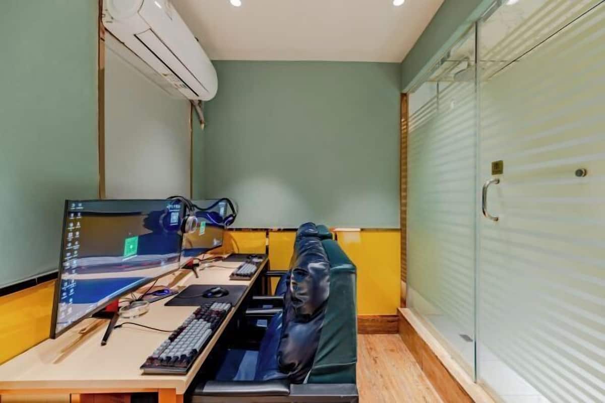 A compact office space with a desk, computer, headphones, and a cushioned seat.