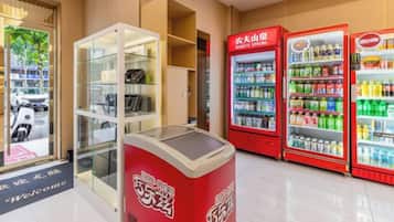 Una máquina expendedora, un expositor de vidrio y dos dispensadores rojos para bebidas en un espacio interior moderno y pulcro.