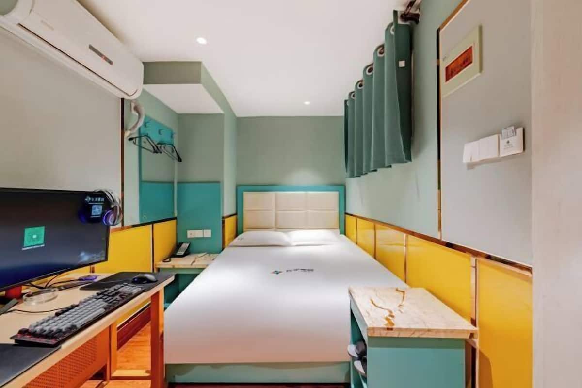 A compact hotel room with a single bed, a desk with a computer, and a television.