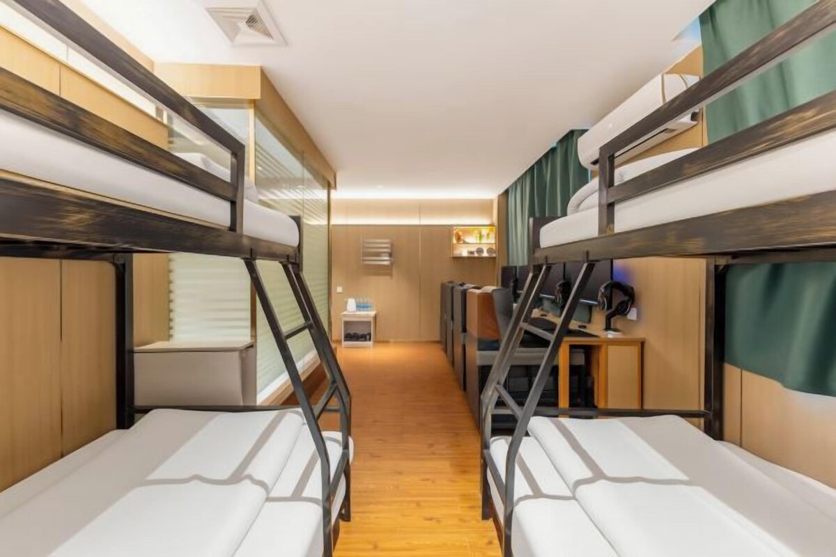 A bunk bed room with a desk and chair, wooden flooring, and a small kitchenette area.