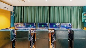 Una habitación con varias estaciones de trabajo, cada una con monitor de computadora, teclado y ratón. Se observa una unidad de aire acondicionado en el techo y una cortina verde al fondo.