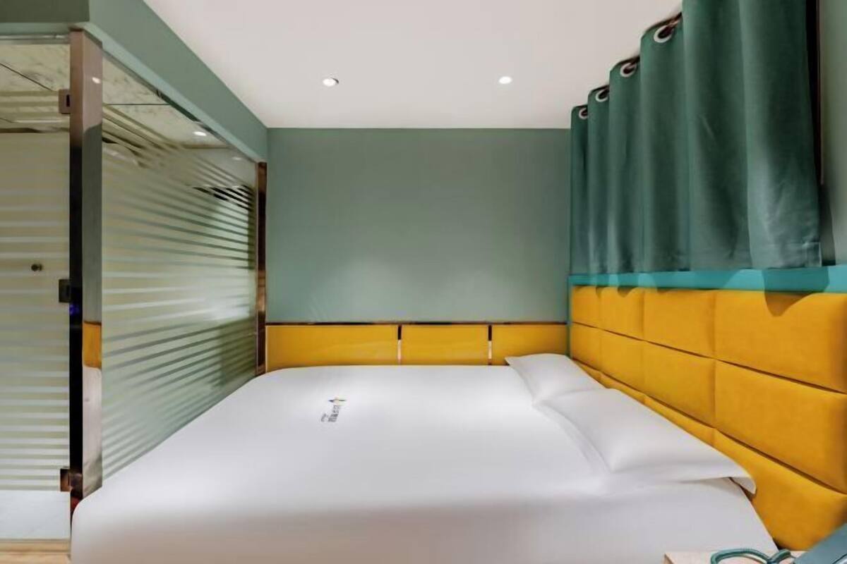 A neatly made bed with a white comforter and pillows, a yellow headboard, and a green curtain.