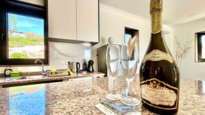 A kitchen with a granite countertop, a bottle of champagne, two glasses, and a window with a view of greenery.