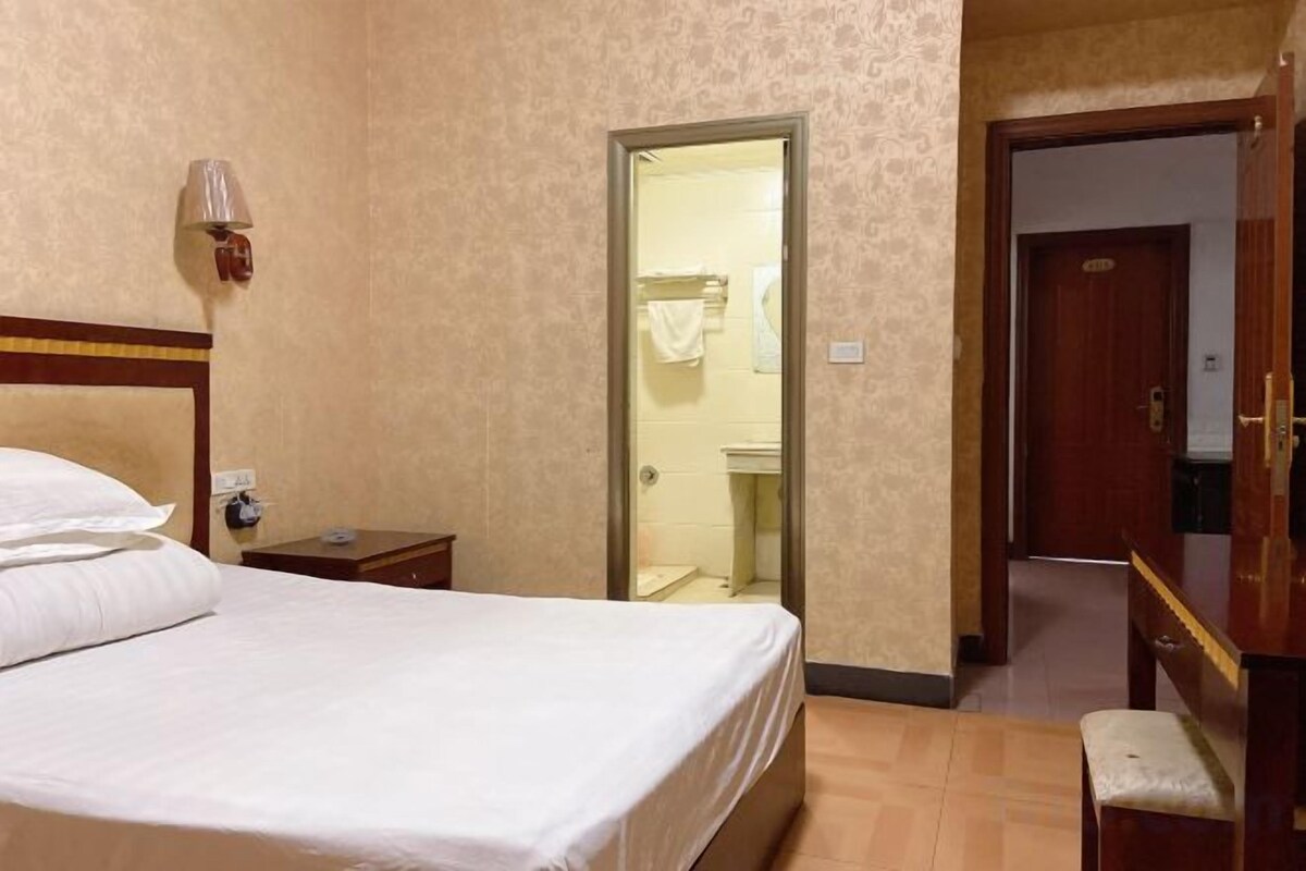 A hotel room with a bed, bedside table, and a mirror. There is a door leading to a bathroom and a hallway.