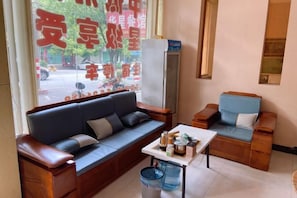 A room with a sofa, a small table, and a chair. There is a window with a view of the street. - Hakka Hotel (Huichang)
