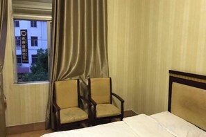 A hotel room with a bed, two armchairs, a window with curtains, and a view of buildings outside. - Hakka Hotel (Huichang)