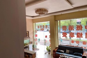 A hotel lobby with a reception desk, seating area, and large windows with a view of the street. - Hakka Hotel (Huichang)
