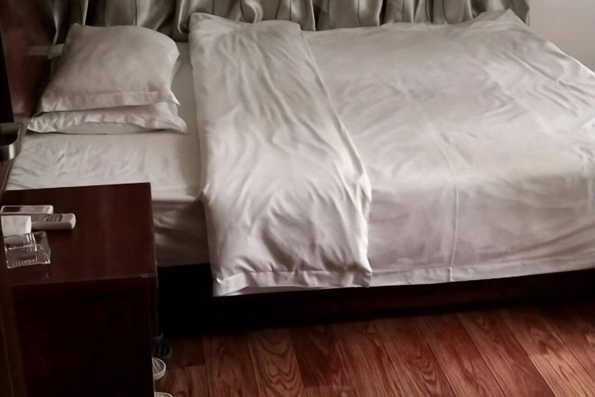 A bed with white bedding, a wooden nightstand with a glass, and a wooden floor.