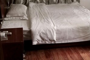 A bed with white bedding, a wooden nightstand with a glass, and a wooden floor. - Huayu Hotel (Qinzhougang) (Qinzhou)