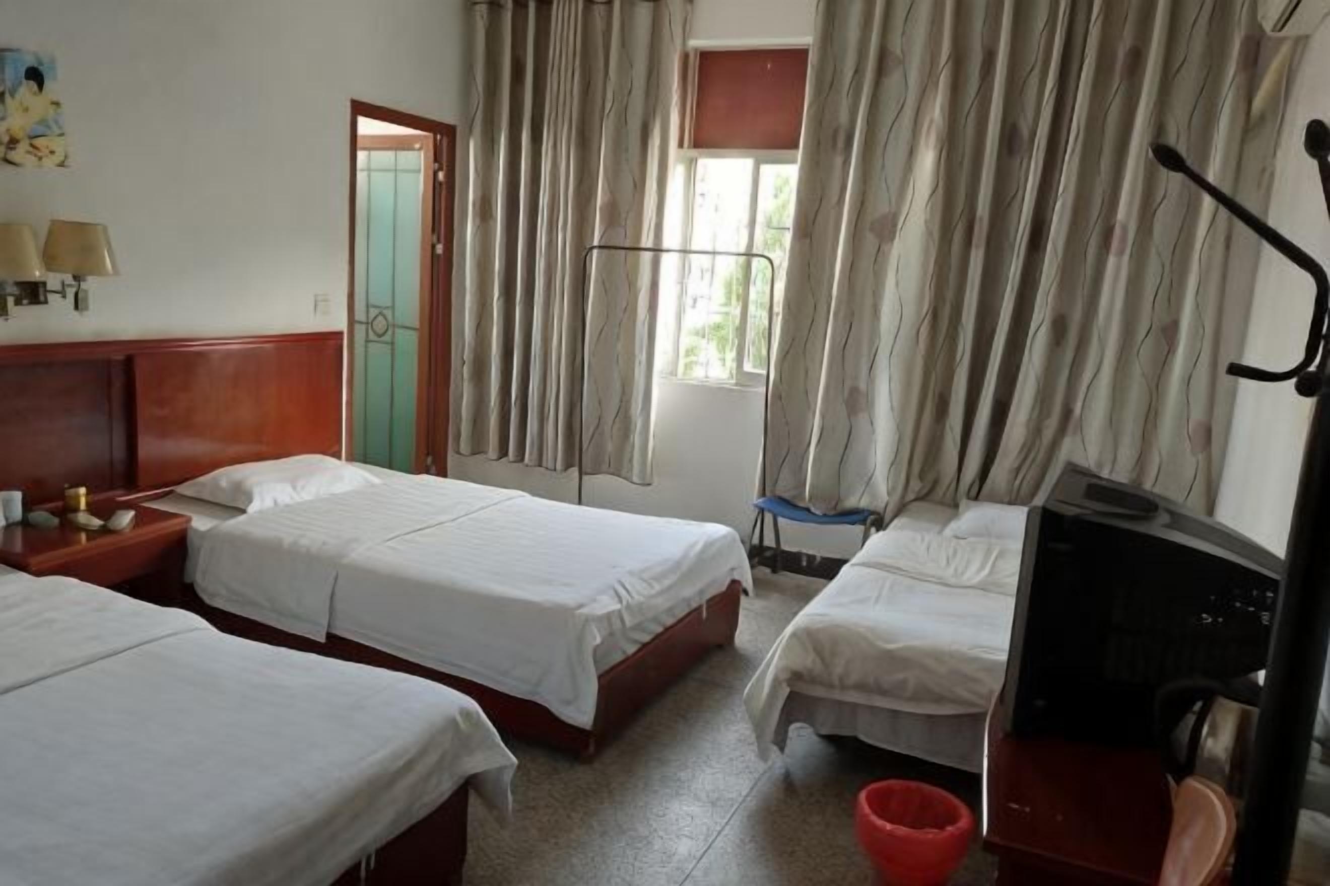 A hotel room with three beds, a desk, a chair, a television, and a window with curtains.