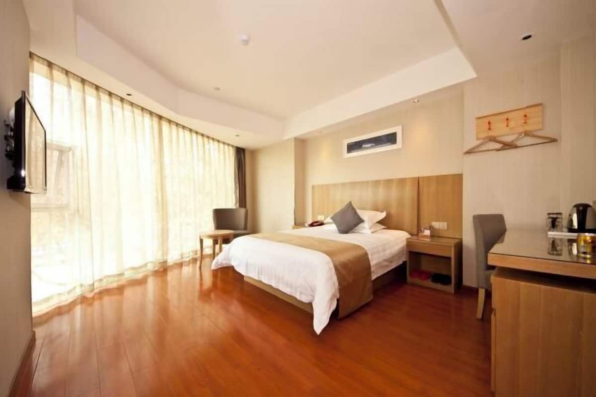 A hotel room with a large bed, a desk, a chair, a TV, and a window with curtains.