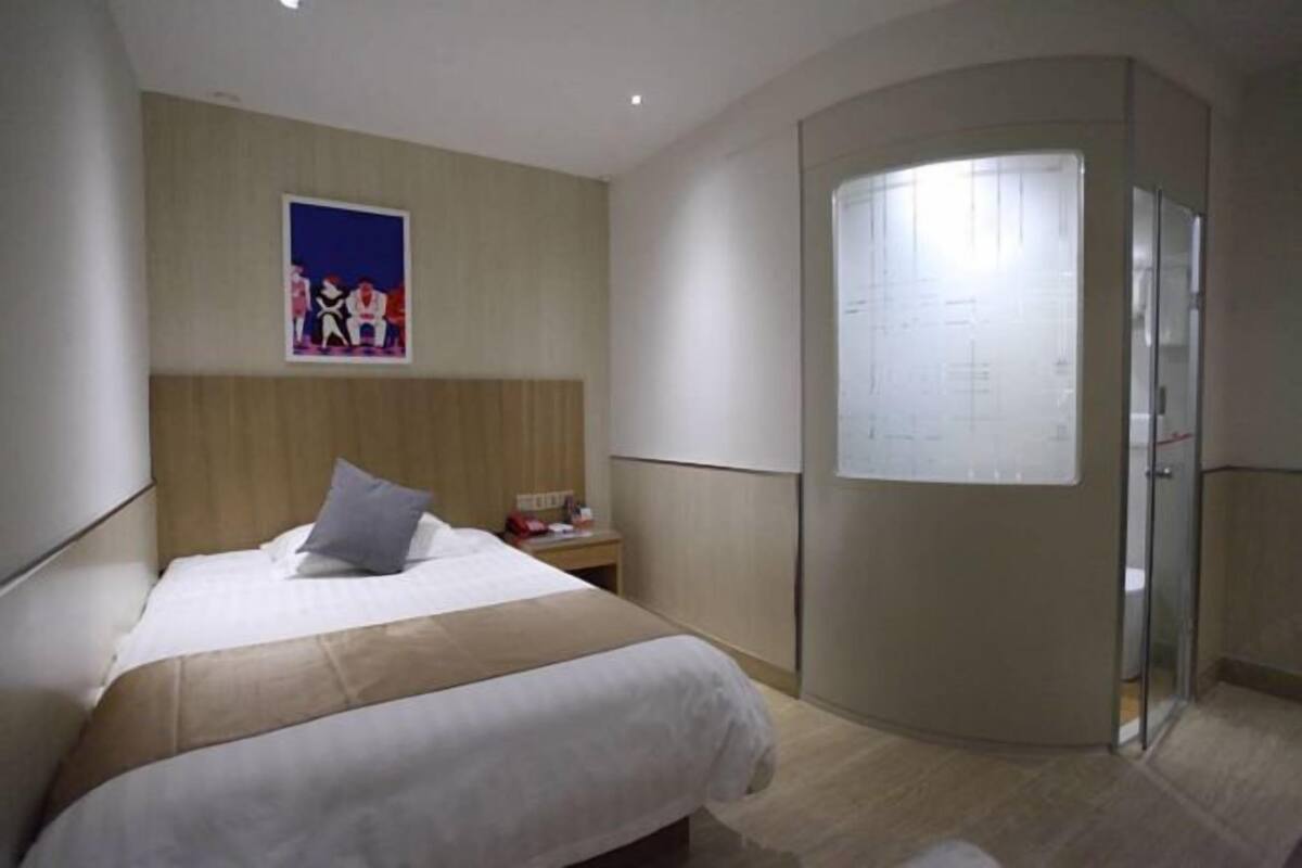 A hotel room with a bed, a nightstand, a poster on the wall, and a glass door leading to a bathroom.