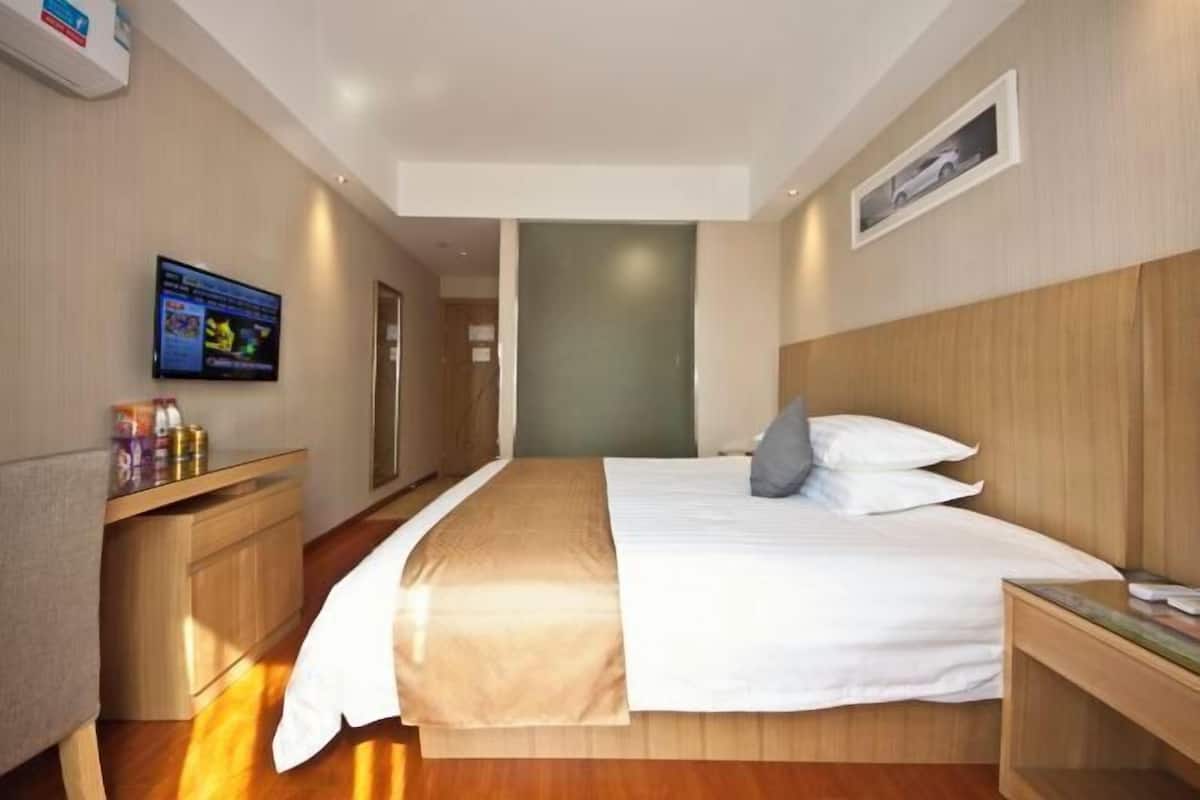 A hotel room with a bed, a TV on the wall, a wooden headboard, and a small bedside table.