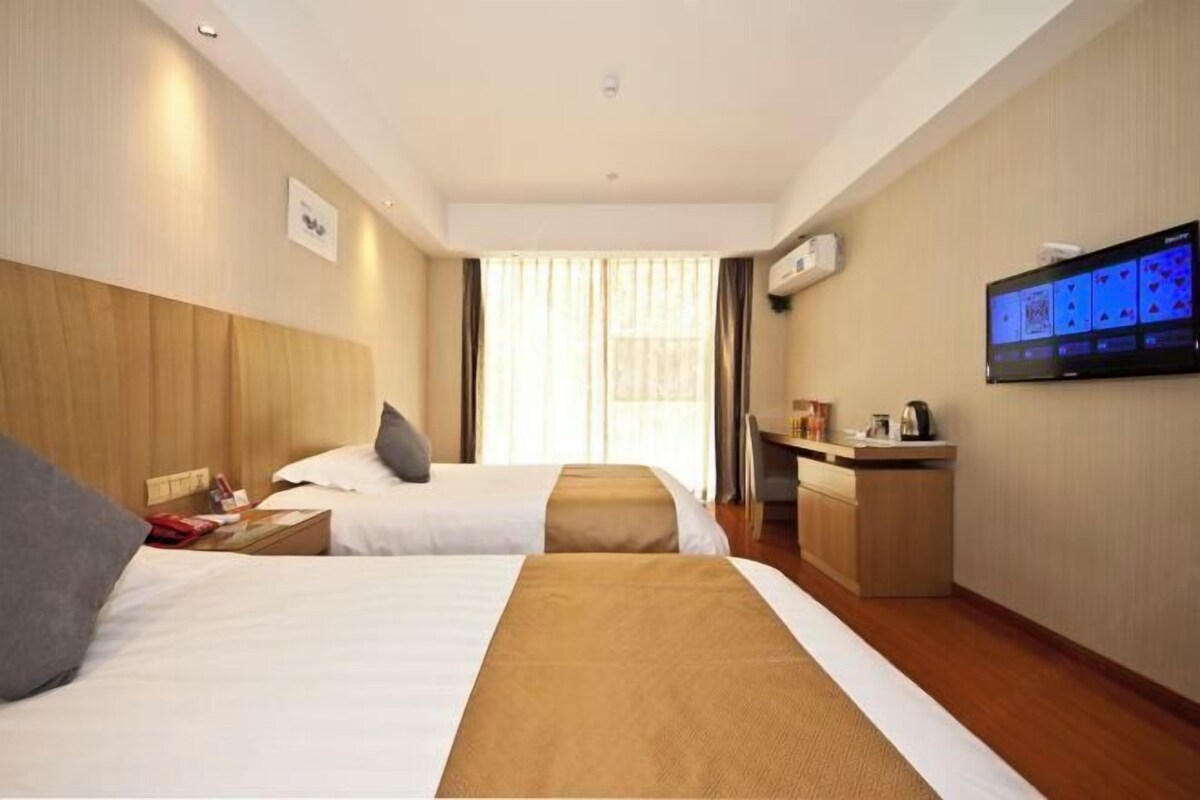 A hotel room with two beds, a desk, a television, and a window with curtains.