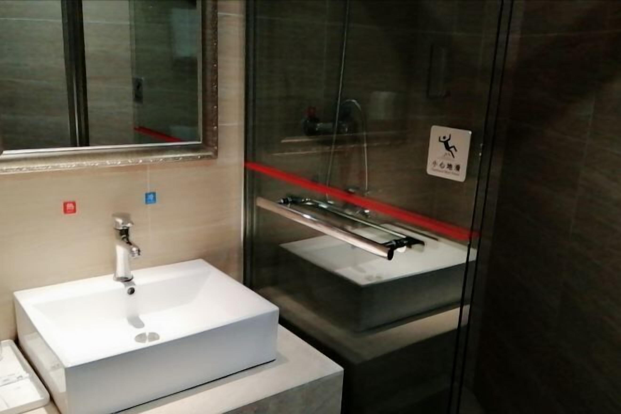 Un baño moderno con lavamanos blanco, cabina de ducha de vidrio y barandilla.