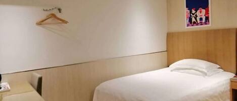 A hotel room with a bed, a desk, a chair, a coat rack, and a painting on the wall.