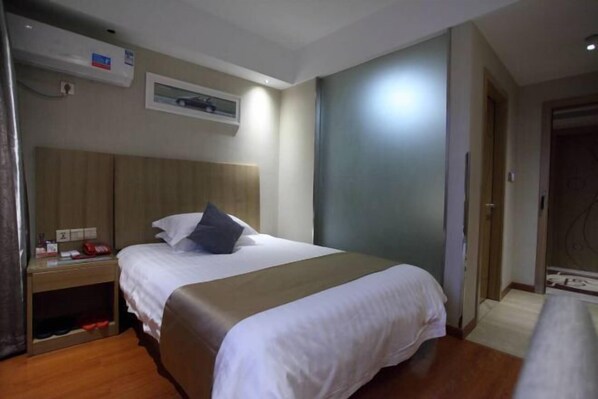 Habitación de hotel con una cama grande, una mesita de noche con lámpara y un aire acondicionado de pared.