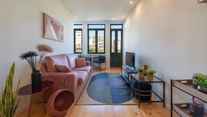 Een moderne woonkamer met een bank, een salontafel, een televisie en een groot raam met uitzicht op gebouwen.