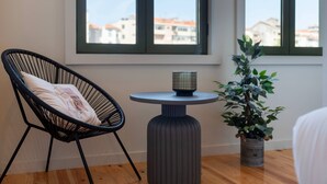 Een kamer met een zwarte frame stoel, een klein rond tafeltje met een kaars, en een bloempot met plant.