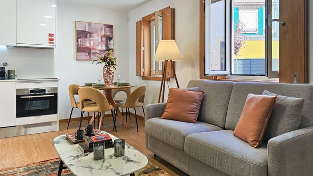 Ein modernes Wohnzimmer mit grauem Sofa, einem Couchtisch und einem Essbereich mit Stühlen und Tisch.