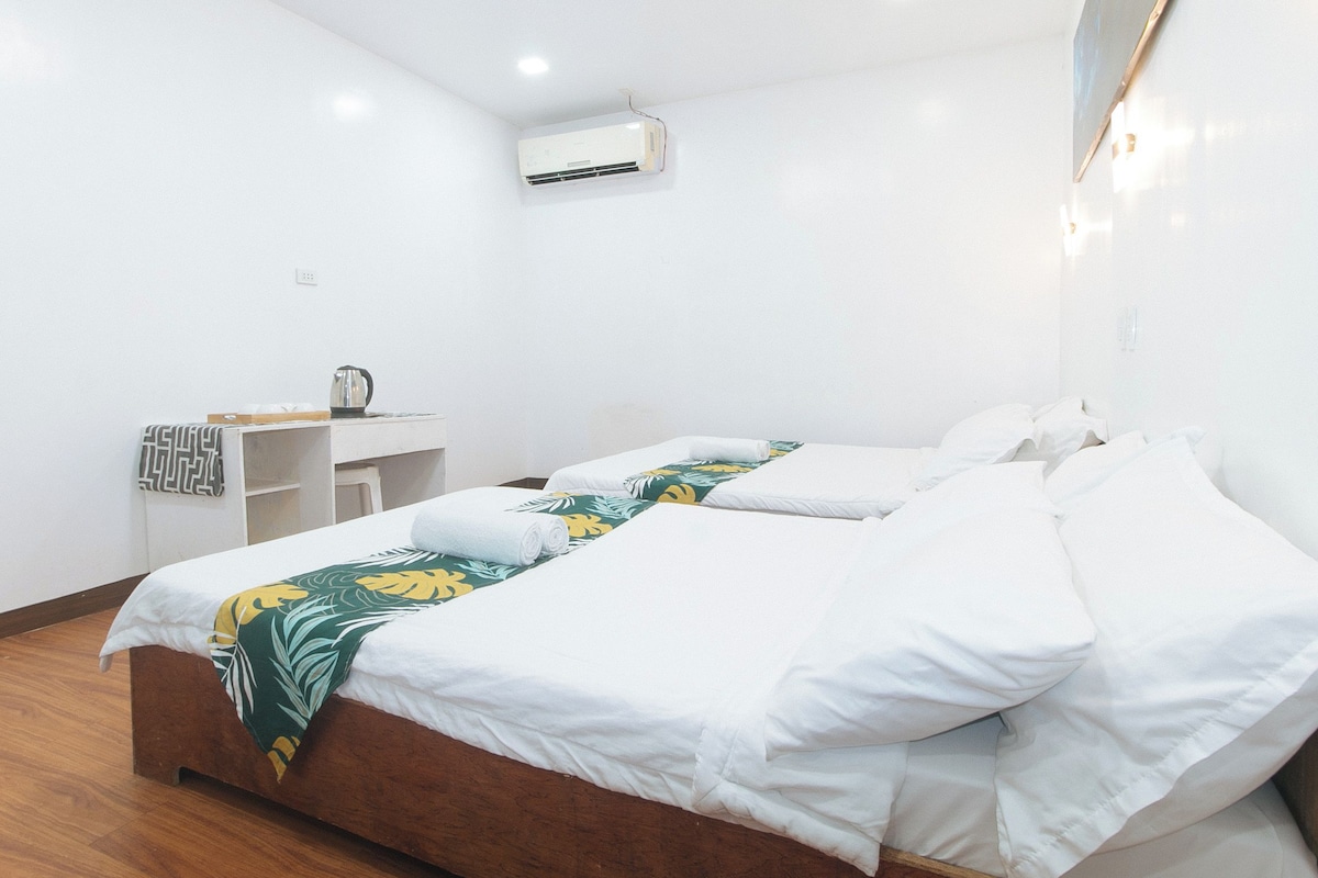 A hotel room with two beds, a desk, and an air conditioning unit.