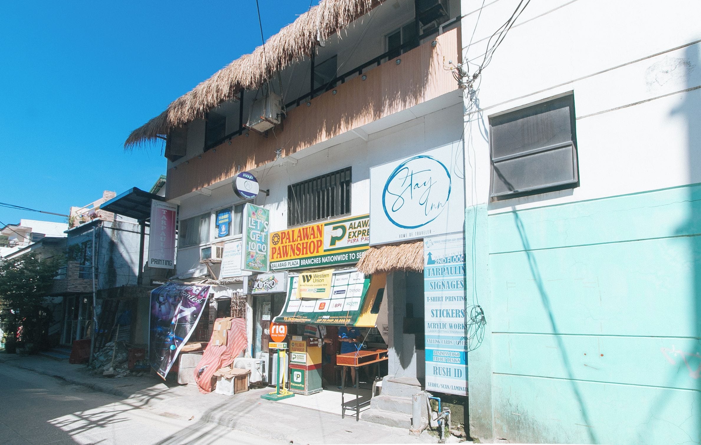 A street view of a building with multiple businesses including a printing shop, a pawnshop, and a cafe.