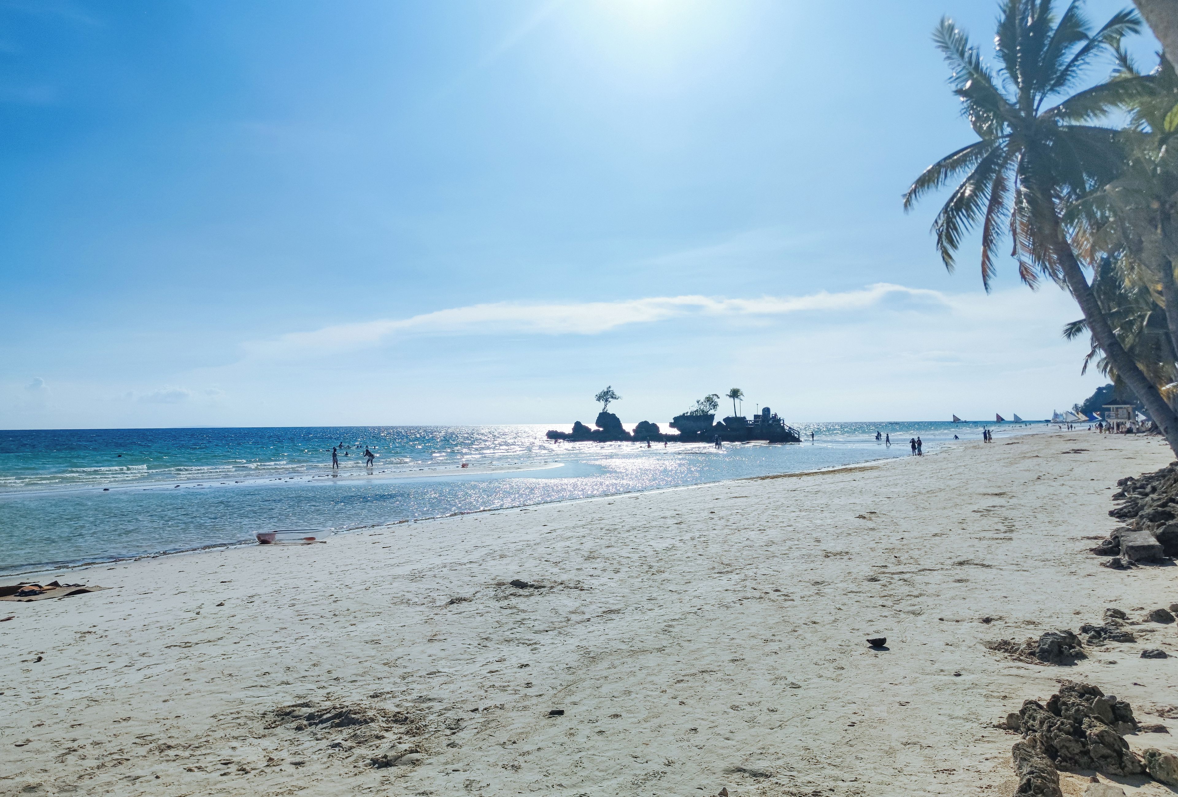 A beach with clear skies, palm trees, and rocky outcrops.