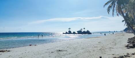A beach with clear skies, palm trees, and rocky outcrops.