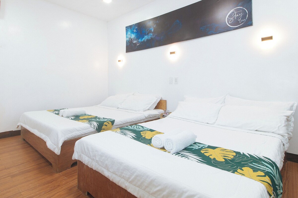 Habitación de hotel con dos camas individuales, suelo de madera, ropa de cama blanca y una manta con motivos tropicales.
