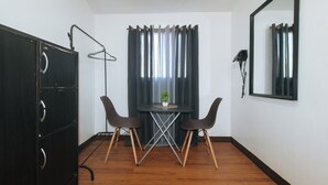 Una habitación pequeña con un armario de madera oscura, una mesa con dos sillas, una planta en maceta y un espejo en la pared.