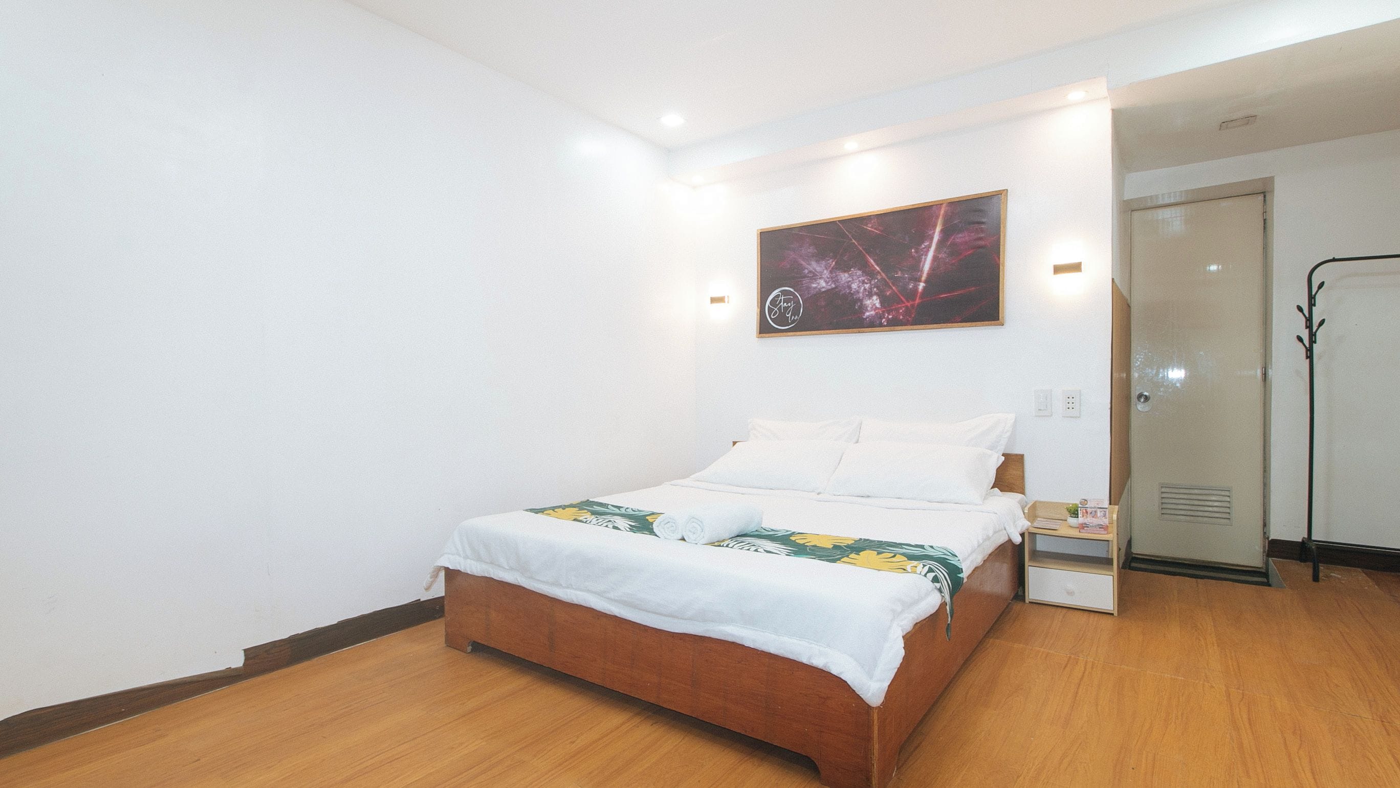 Une chambre d’hôtel avec un lit, une table de chevet, un porte-manteau et une porte.