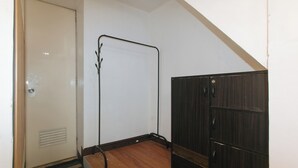 Una habitación con piso de madera, una puerta blanca, un perchero de metal negro y un armario de madera oscura.
