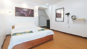 A hotel room with a wooden bed, a painting on the wall, a mirror, and a shelf with a kettle. - Stay Inn Station 1 Boracay By Reddoorz (Boracay Island)
