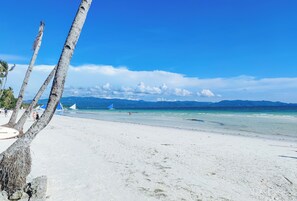 Una playa de arena blanca, palmeras y cielo azul despejado.