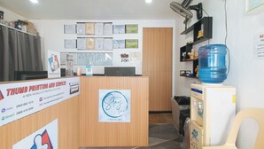 Un mostrador de recepción con un cartel que dice 'Thumb Printing and Services', una pared con diplomas, un dispensador de agua y un ventilador.