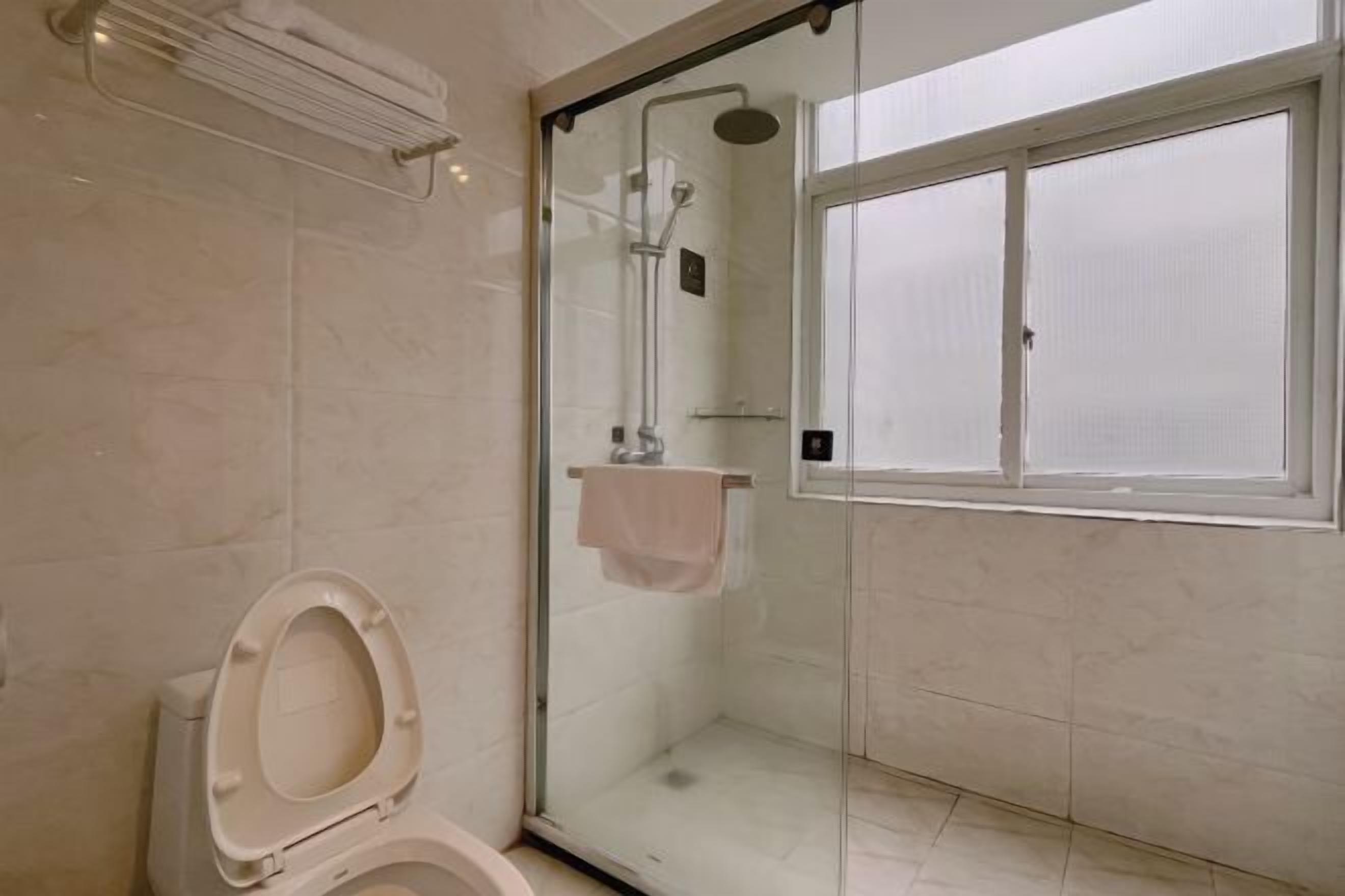 A modern bathroom with a glass-enclosed shower, a toilet, and a window.