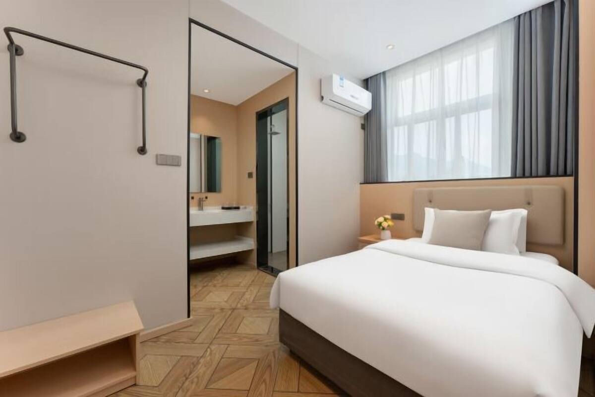 Hotellihuone, jossa on sänky, kylpyhuone peilillä ja ilmastointilaite.